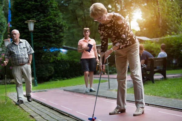 Female pensioner at a minigolf court hits a ball with an standard racket — Stock Photo, Image