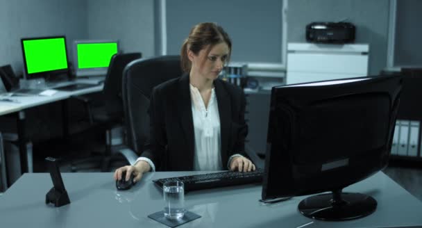 4K: Una joven está sentada en su computadora. Ella está tomando un trago de agua mientras trabaja y se complace en el trabajo — Vídeo de stock