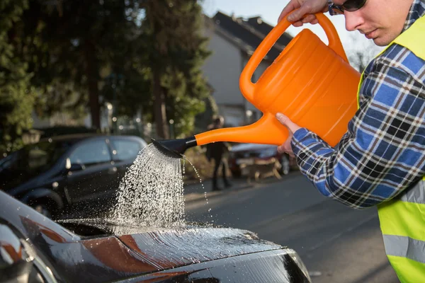 En ung man använder en vattenkanna för att rengöra sin bil — Stockfoto