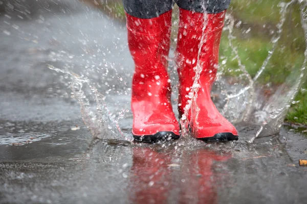 Red rubber boots are jumping into a big puddle — Stock Photo, Image