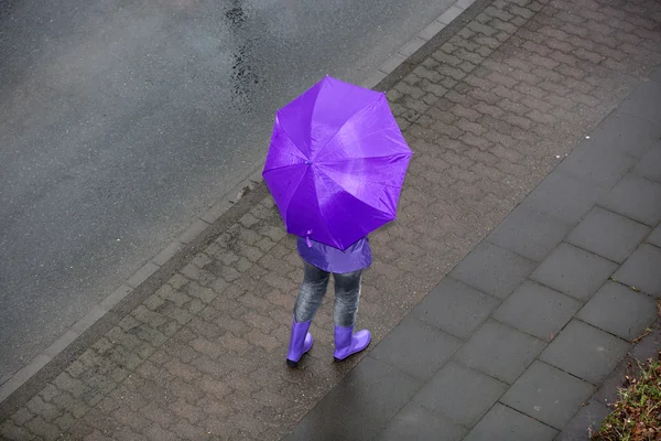 Mulher está de pé na chuva com um guarda-chuva roxo — Fotografia de Stock