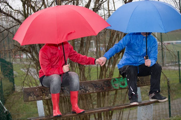 Mano en mano sentada en el banco del parque bajo la lluvia —  Fotos de Stock