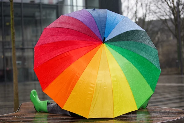 Seduto sotto la pioggia, coperto da un ombrello colorato . — Foto Stock