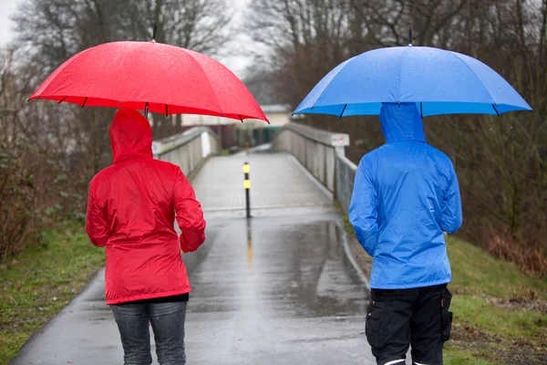 Bir erkek ve kadın ile yağmurluk giymiş yağmurda yürüyorsun — Stok fotoğraf