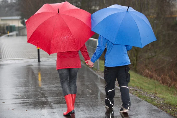 Casal andar de mãos dadas através da chuva . — Fotografia de Stock