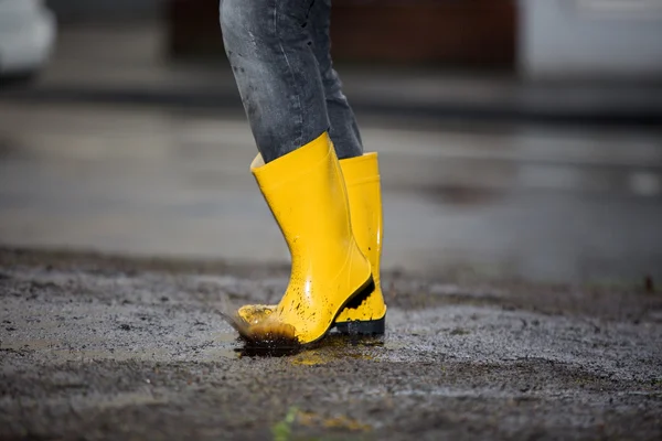 Gelbe Gummistiefel in einer schmutzigen Pfütze — Stockfoto