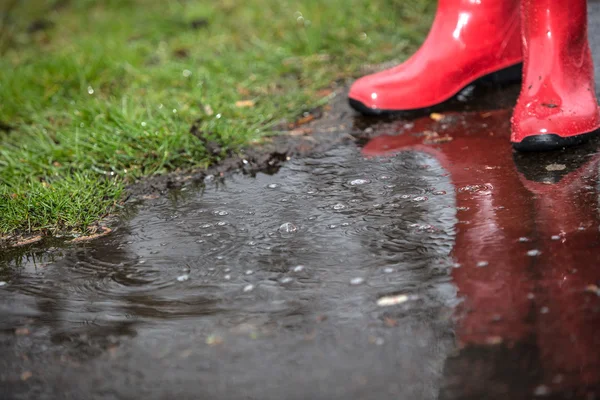 Botas vermelhas em uma poça com gotas de água — Fotografia de Stock