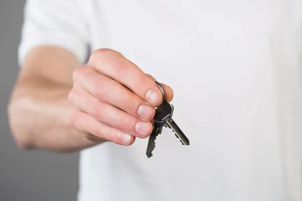 A mans hand houdt een sleutel-pair, geïsoleerd op een grijze achtergrond — Stockfoto