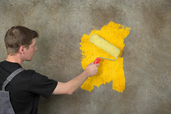 Painter repaints a structured wall in yellow with a color roller — Stock Photo, Image