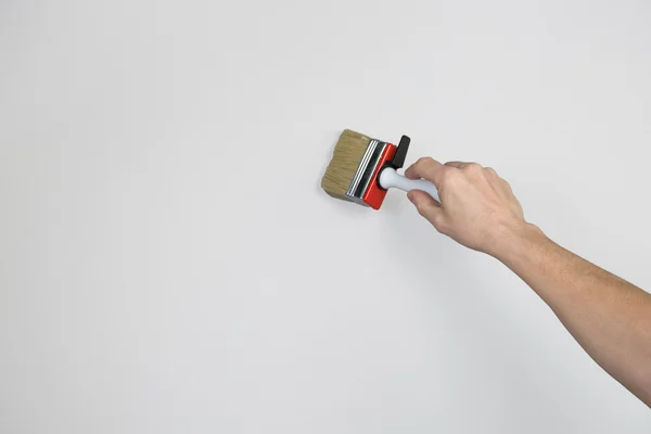 A mans arm with a paint brush on a grey wall. — Stock Photo, Image