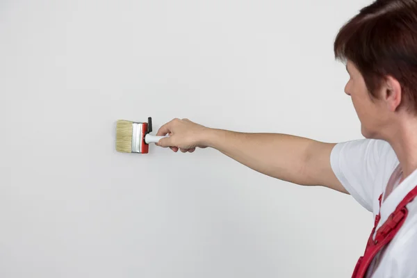 Mulher está pintando uma parede cinza com um pincel de tinta — Fotografia de Stock
