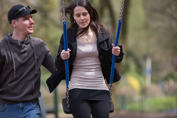 Jong paar is met behulp van een schommel op een playgound. — Stockfoto