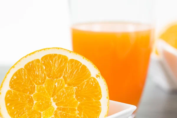 Sliced orange fruit with a glass of orange juice in the backgrou — Stock Photo, Image
