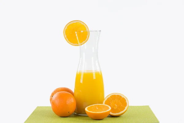Big glass carafe with orange juice on a green table runner, deco — Stock Photo, Image