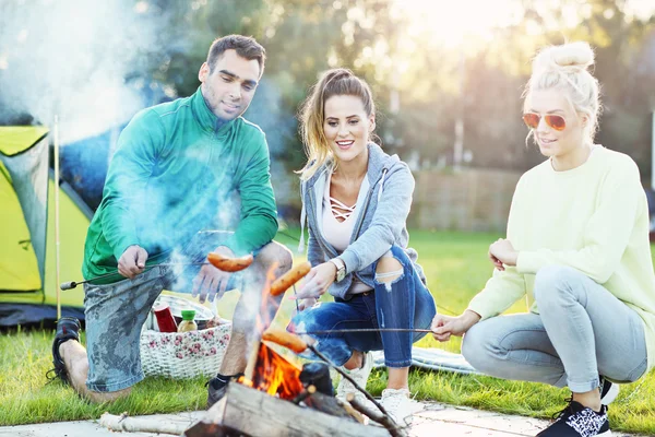 Amici che preparano salsicce sul falò — Foto Stock