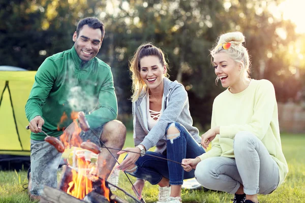 Amici che preparano salsicce sul falò — Foto Stock