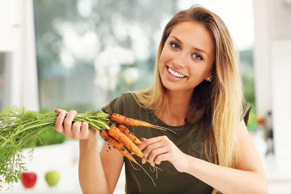 Woman with fresh carrots in kitchen — Stock Photo, Image