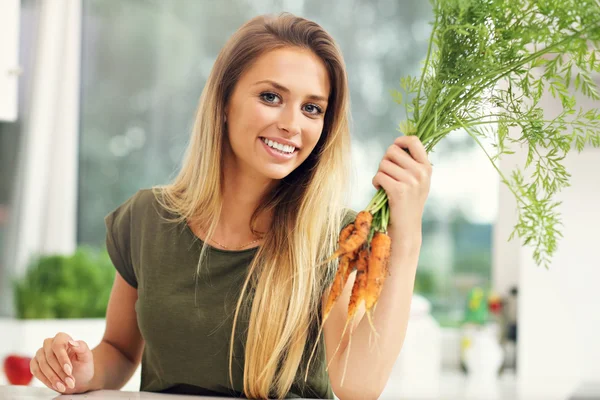 Woman with fresh carrots in kitchen — Stock Photo, Image