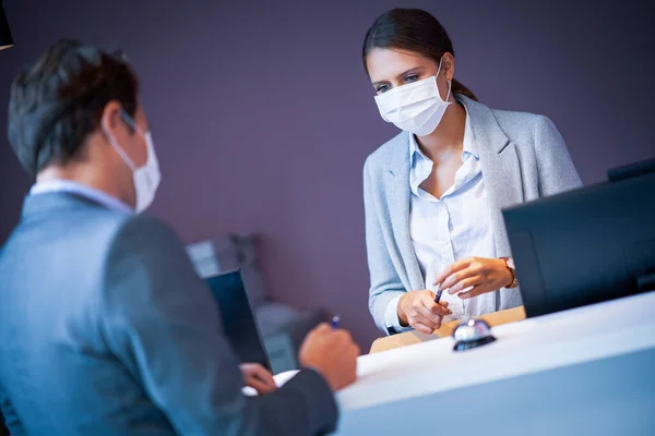 Egy maszkos üzletember bejelentkezik egy hotel recepciójára. — Stock Fotó