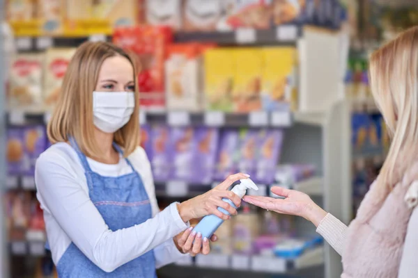 Vuxen kvinna i medicinsk mask med handdesinfektionsmedel innan du handlar livsmedel — Stockfoto