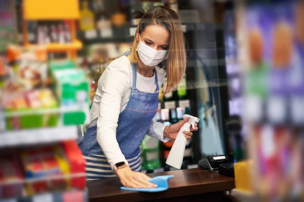 Assistente de loja desinfetando superfícies em mercearia — Fotografia de Stock