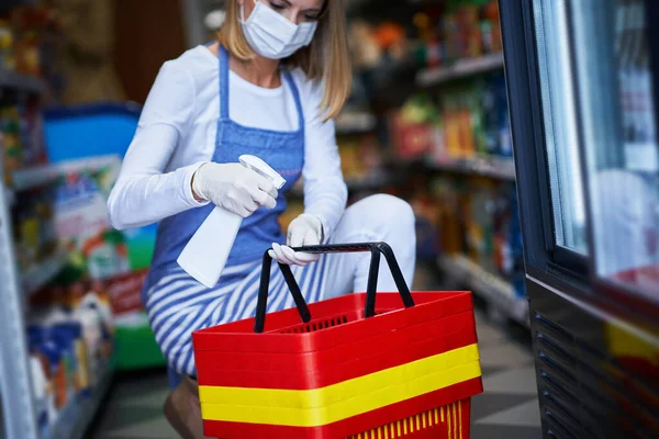 Assistente de loja trabalhando em máscara médica desinfetando carrinhos — Fotografia de Stock