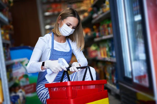 Assistente de loja trabalhando em máscara médica desinfetando carrinhos — Fotografia de Stock