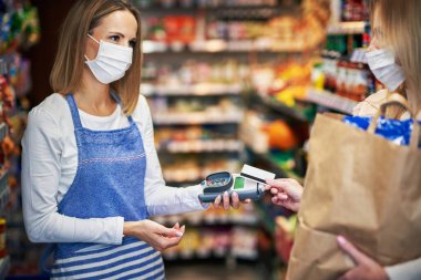 Tıbbi maskeli yetişkin bir kadın marketten sipariş alıyor.