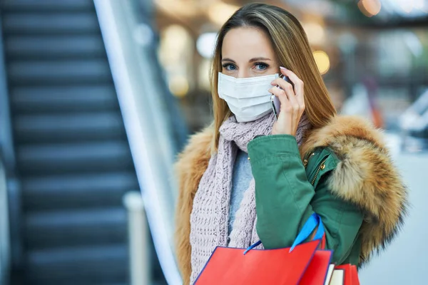 Portrait of adult woman shopping in mall using smartphone wearing a mask — Stock Photo, Image