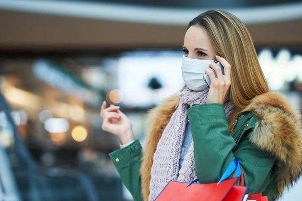 Portrait of adult woman shopping in mall using smartphone wearing a mask — Stock Photo, Image