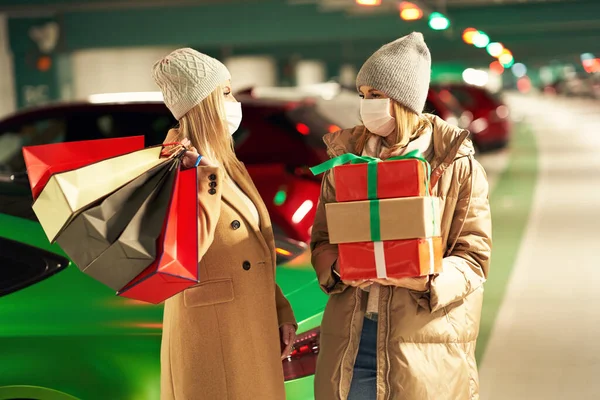 Two women with shopping bags in masks in underground parking lot