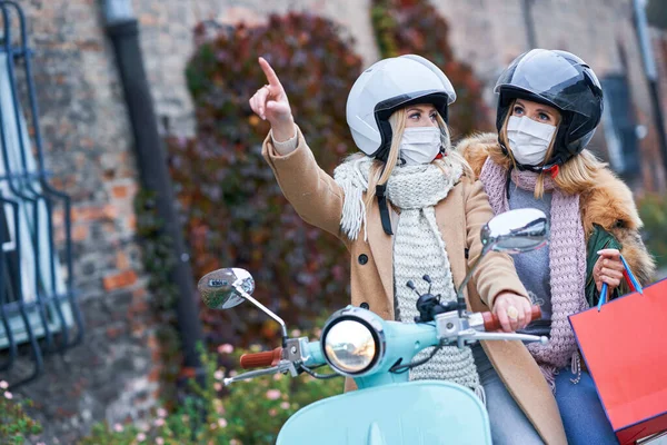 Duas mulheres usando máscaras e segurando sacos de compras em scooter — Fotografia de Stock