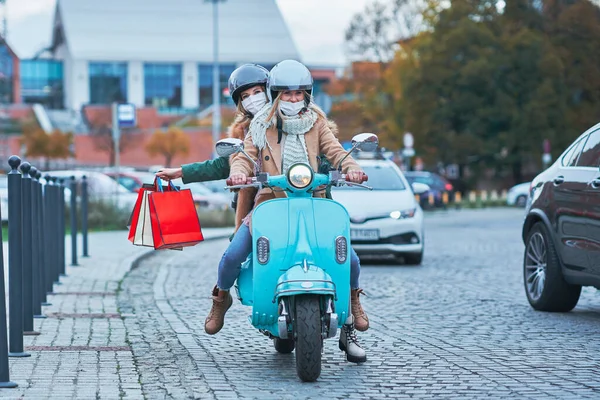 Twee vrouwen dragen maskers en houden boodschappentassen op scooter — Stockfoto