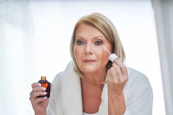 Senior woman using anti wrinkle serum in the bathroom — Stock Photo, Image