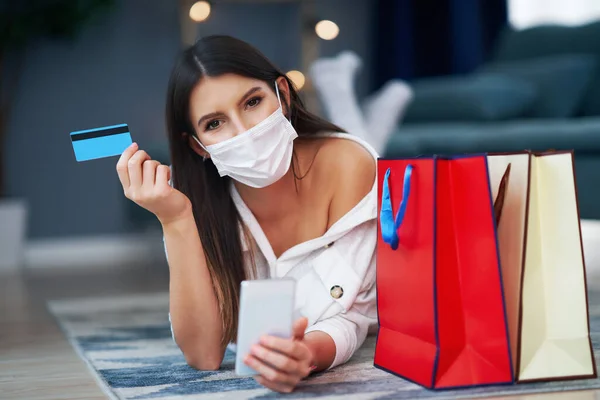Maskeli güzel kadın internetten kredi kartıyla alışveriş yapıyor. — Stok fotoğraf