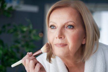 Banyoda makyaj yapan yaşlı bir kadın.