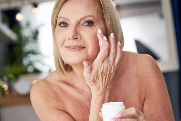Старша жінка використовує крем проти зморшок у ванній — стокове фото