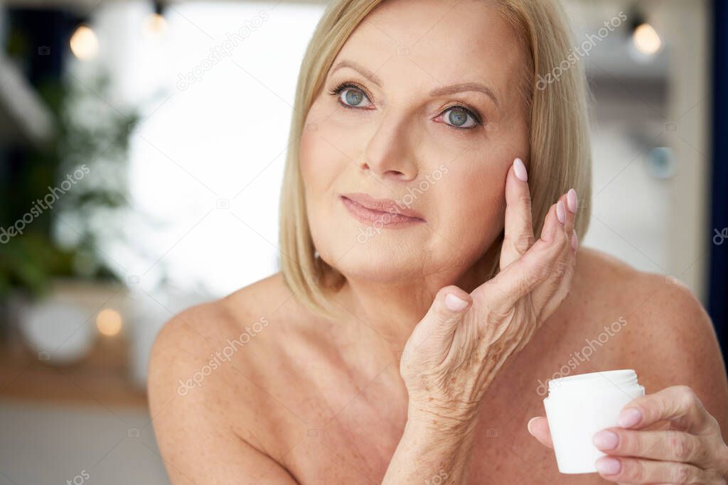 Senior woman using anti wrinkle cream in the bathroom