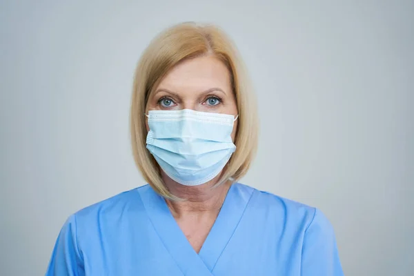 Médica sênior posando em máscara sobre fundo cinza — Fotografia de Stock