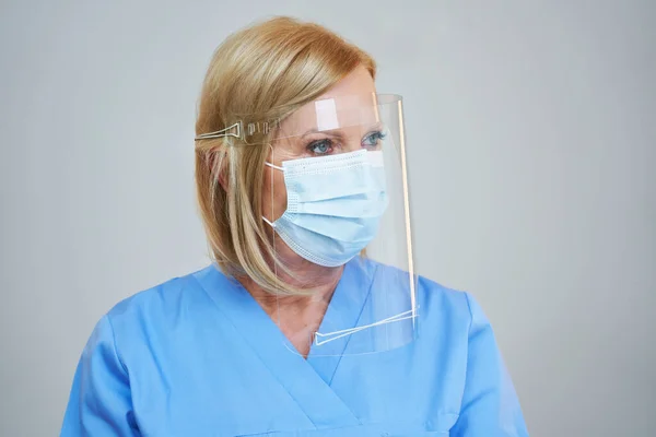 Senior female doctor posing in mask and shield over gray background — Stock fotografie