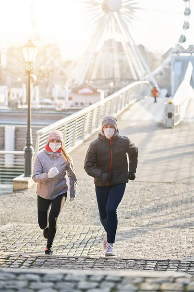 Erwachsenes Paar joggt während der Sperrung maskiert durch die Stadt — Stockfoto
