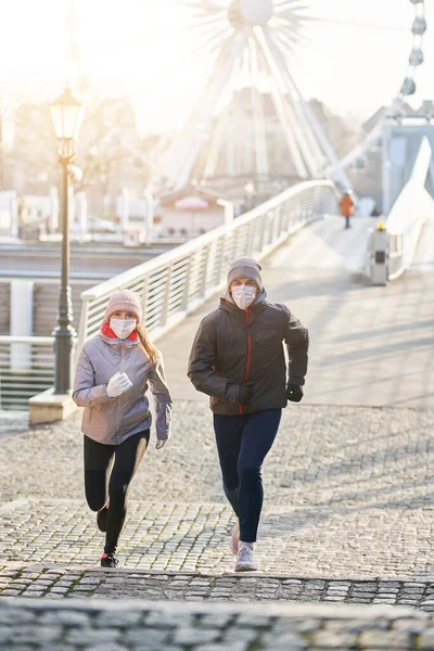 Pareja adulta corriendo en la ciudad con máscaras durante el encierro — Foto de Stock