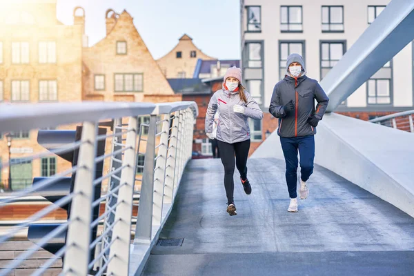 Dospělí pár jogging ve městě v maskách během uzamčení — Stock fotografie