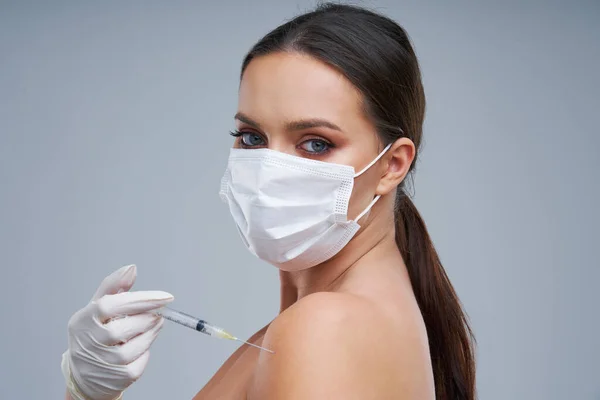 Portrét krásné ženy držící vakcínu v masce na šedém pozadí — Stock fotografie