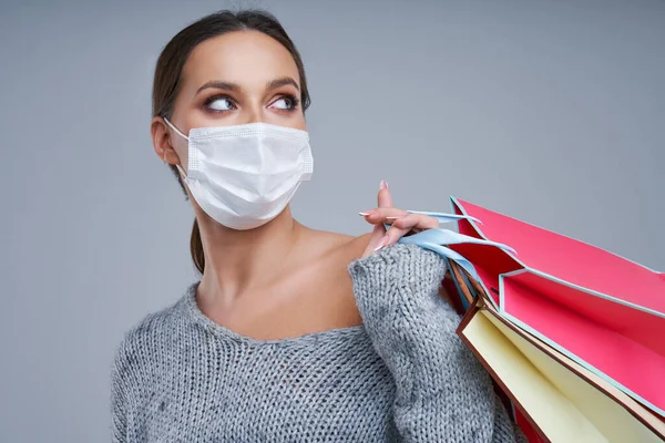 Portrait of beautiful woman in mask holding shopping bags on gray background — Stock Photo, Image