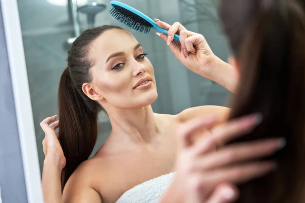 Frau bürstet nach der Dusche Haare im Badezimmer — Stockfoto