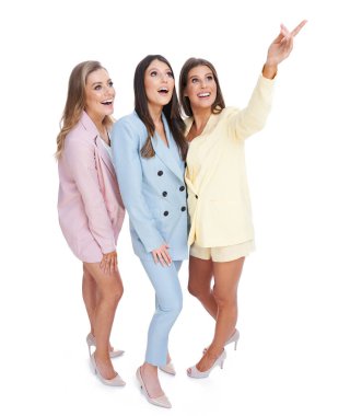 Beyaz arka planda poz veren pastel elbiseli üç kadın.