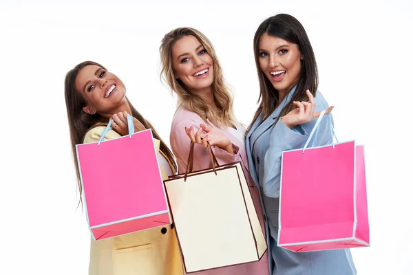 Três mulheres em ternos pastel segurando sacos de compras sobre fundo branco — Fotografia de Stock