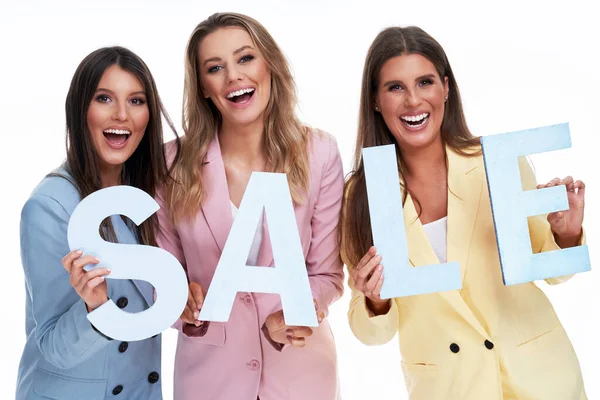 Three women in pastel suits holding sale letters over white background — Stock Photo, Image