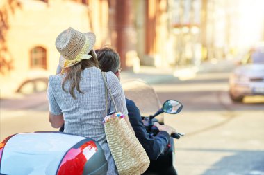Mutlu, olgun bir çift güneşli bir günde şehirde scooter kullanıyor.
